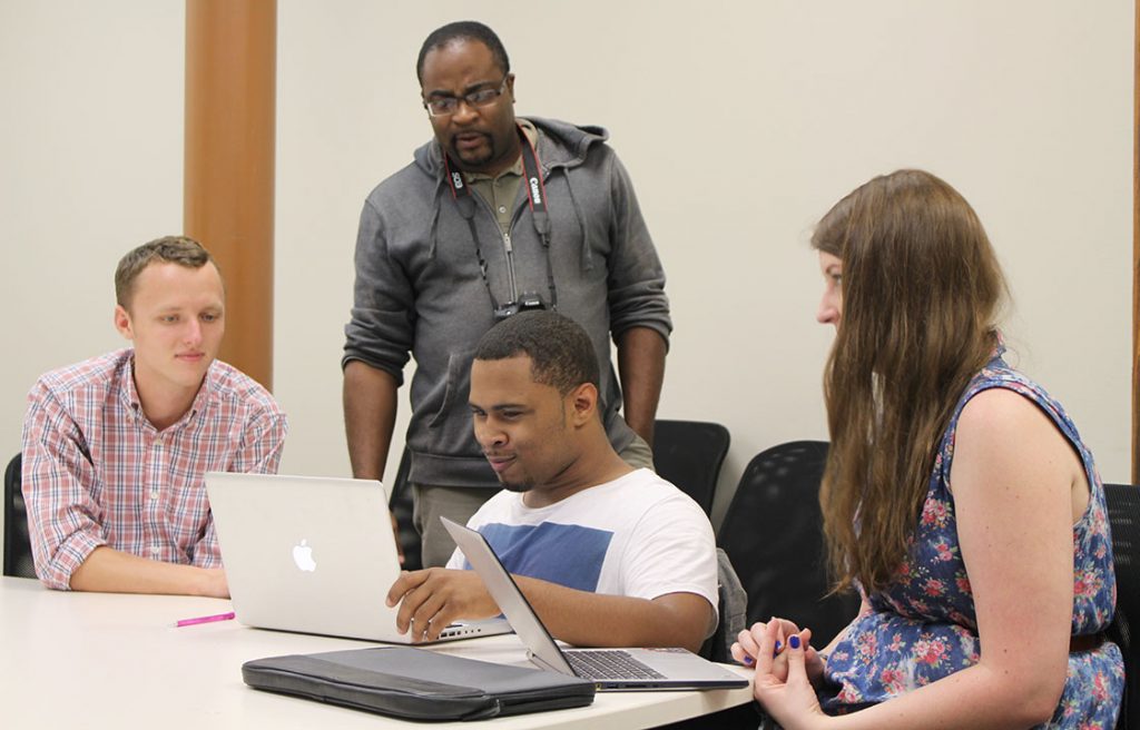 Teen Mentoring Coordinator Carlton Koonce looks on as UNC mentors, left to right, Eric Surber and Sarah DeWeese work with Partners for Youth Intern Christian Frazier on his story. (Staff photo by Gwen )