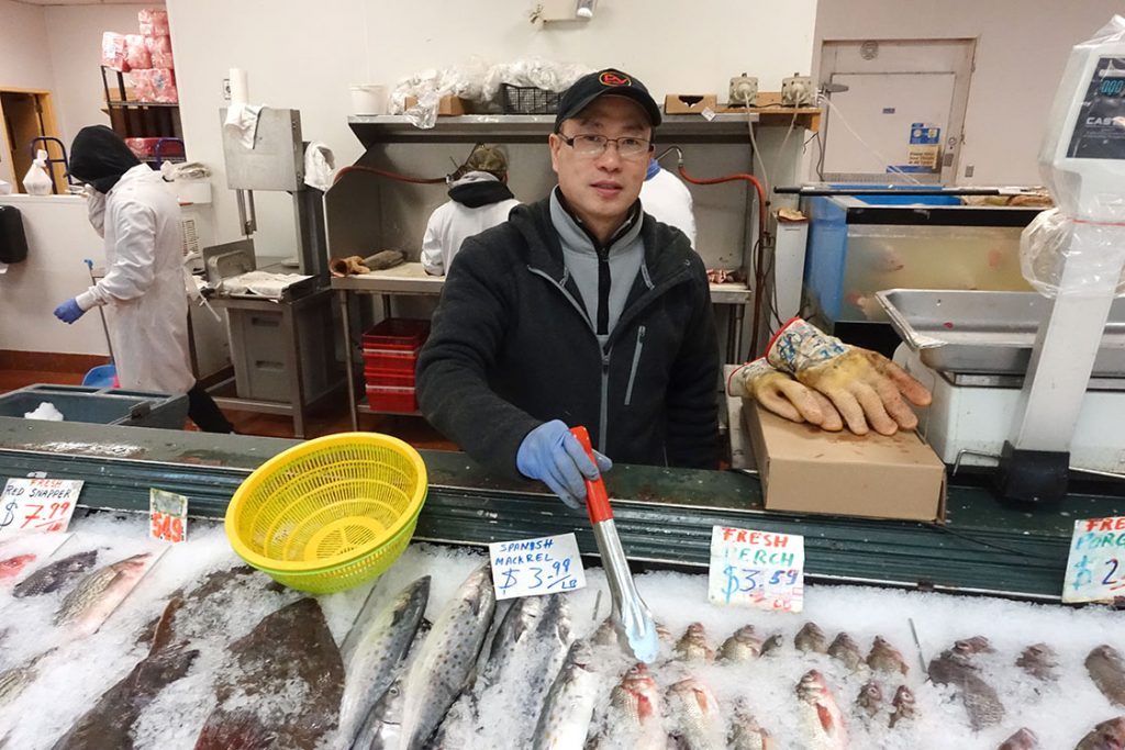 Zulin Yang, the general manager of LiMing's Global Mart in Durham, introduces the different kinds of fish to his customers. (Staff photo by Mengqi Jiang)