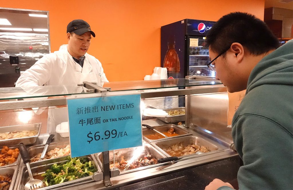 Simon Young, the employee at LiMing’s Global Mart, is packaging cafeteria-style food for customers. (Staff photo by Mengqi Jiang)  