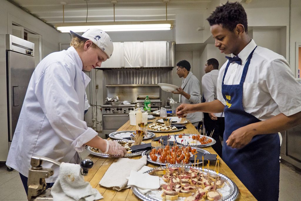 Kaleb Shaw-lunsford (right) picks up a plate of candied tomatoes prepared by James Betts (left) to cater to get guests waiting in the lobby. “The tomatoes are caramelized and dipped into parsley. It’s a cool combination of flavors, and we made them,” says Betts with excitement about keeping the food stocked. (Staff photo by Cole McCauley)